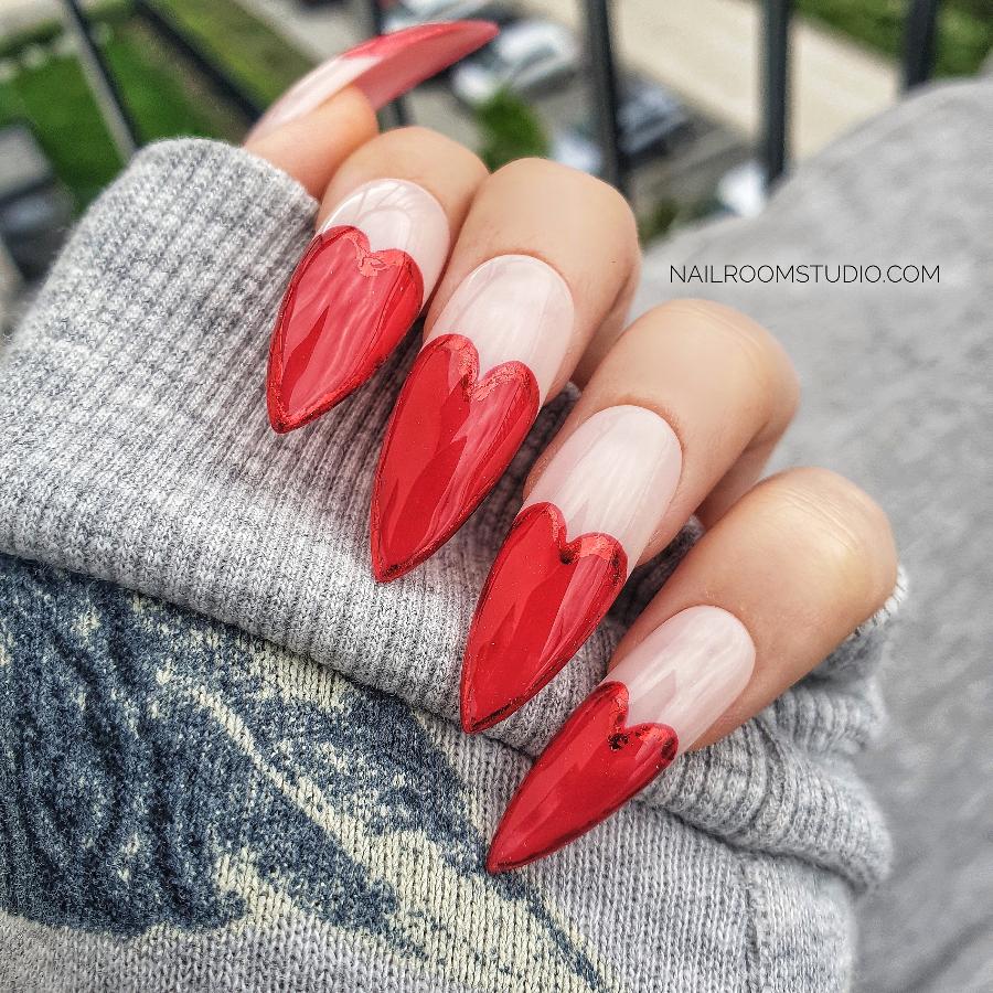 Soft pink press-on nails with red chrome heart-shaped French tips, a feminine and romantic look, ideal for dates or Valentine's Day, displayed on hands