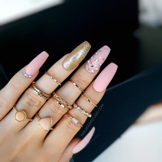 Elegant powder pink matte nails enhanced with sparkling gold glitter and opal Swarovski crystals for a dazzling effect